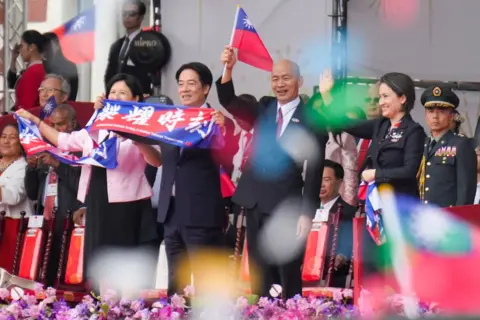 Getty Images O presidente de Taiwan, Lai Ching-te, a primeira-dama Wu Mei-ju, o vice-presidente de Taiwan, Hsiao Bi-khim, e o presidente do Yuan Legislativo de Taiwan, Han Kuo-yu, acenam durante as celebrações do Dia Nacional em frente ao Gabinete Presidencial em Taipei