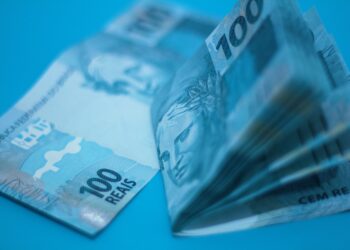 Pilha de cédulas de 100 reais sobre superfície azul, ilustrando a inflação medida pelo IPCA-15